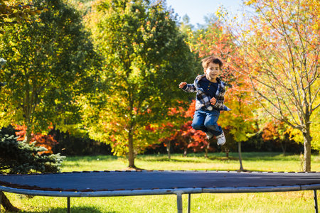 Happy boy jumping on a trampoline in the backyard surrounded by colorful autumn treesの写真素材