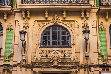Facade of an ornate historic building in Alicante, Spain, featuring elegant wrought iron balconies, pastel green tiles, and decorative window moldings in modernist style.の写真素材