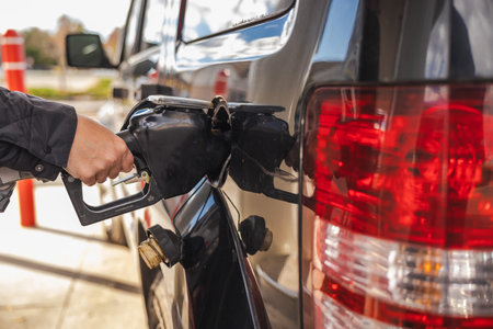 Person refills vehicle with fuel at a gas station, holding the nozzle while topping up the tank