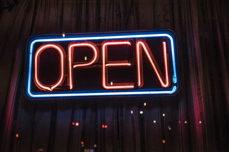 Bright neon open sign glowing in red and blue colors at night on a storefront window.の写真素材