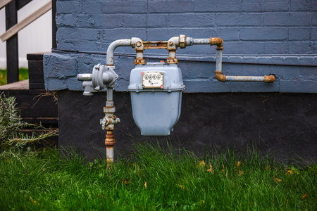 Residential natural gas meter and pipeline system attached to a brick house wall with green grass in the foreground.の写真素材