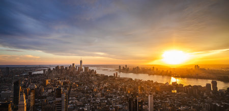 Aerial panoramic view of New York City skyline at sunset with golden sunlight reflecting on the Hudson River and modern skyscrapers glowing in evening lightの写真素材