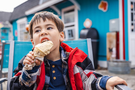 Boy in a red jacket enjoying ice cream outdoors in front of a colorful cafeの写真素材