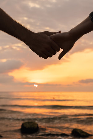 Silhouette of two people holding hands at sunrise by the sea, symbolizing love, trust, and connection in a calm and romantic morning atmosphereの写真素材