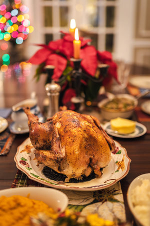 Christmas roasted turkey served on a festive holiday table with candles, poinsettia, colorful lights, and traditional side dishes.の写真素材