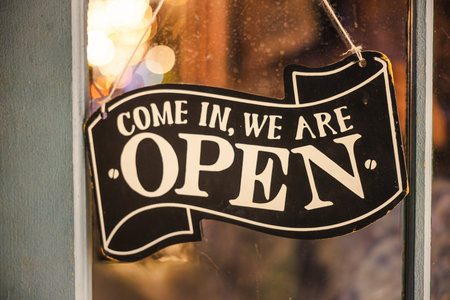 Closeup of a vintage open sign hanging on a shop window with warm bokeh lights in the background.の写真素材