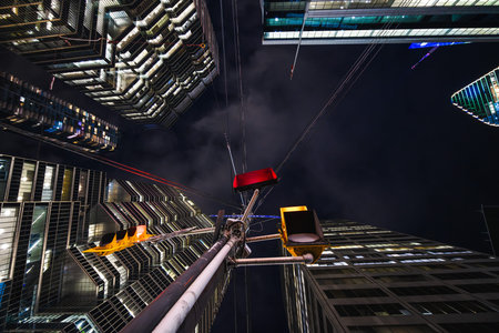 A red traffic signal hangs like a suspended ember between towering glass facades, while cables...