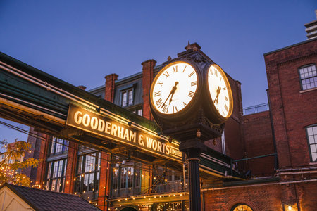 Toronto, Canada, October 20, 2025: Evening view of the illuminated Gooderham and Worts clock in the Distillery District, surrounded by historic brick buildings and festive string lights.のeditorial素材