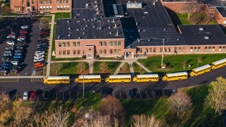 Aerial shot of an American school campus with yellow school buses lined up outside, surrounded by...