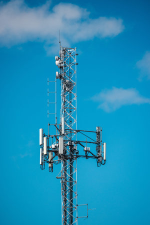 Cellular tower with multiple antennas and telecom equipment against bright blue sky