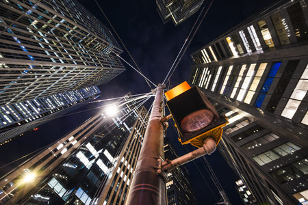 Nighttime upward view of towering glass buildings converging above a glowing traffic light, creating...