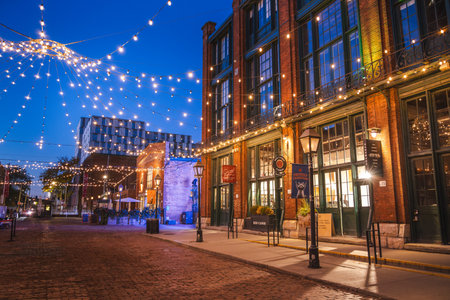 Toronto, Canada, 20 October 2025: Evening street view of the historic Distillery District with brick buildings and festive string lights over the cobblestone walkway.のeditorial素材