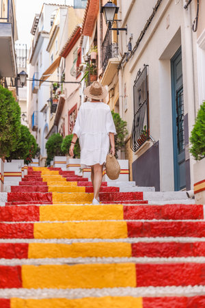 Young woman in a white dress walking up the colourful Spanish Steps in the Arrabal old town district of Calpe, Spainの写真素材