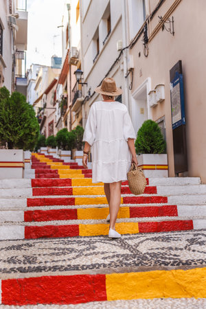 Young woman in a white dress walking up the colourful Spanish Steps in the Arrabal old town of Calpe, Spainの写真素材