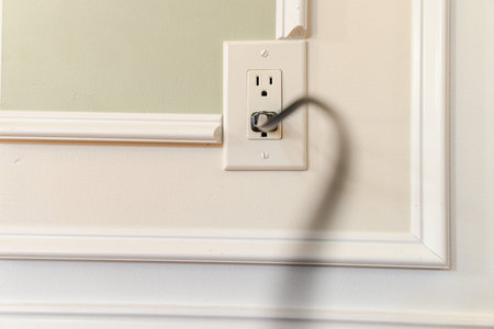 Blurred power cable plugged into American wall outlet on decorative interior wall with white molding...