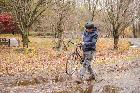 Man carrying bicycle on muddy autumn path after rainの写真素材