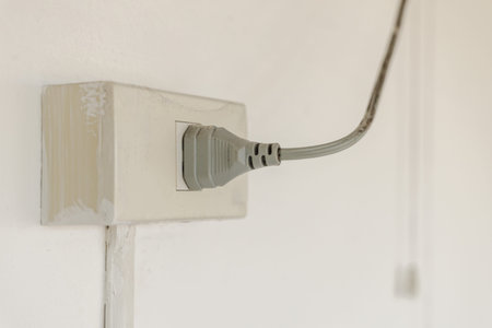 Electric plug connected to wall socket on white wall, household power outlet with cable supplying...