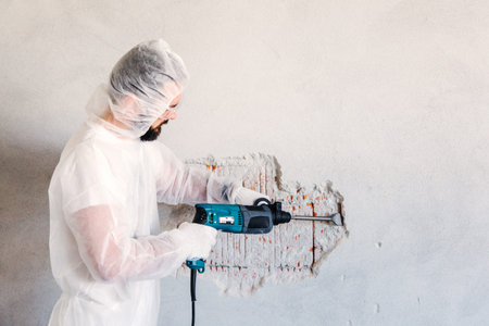 Worker removes plaster from a brick wall with a perforator