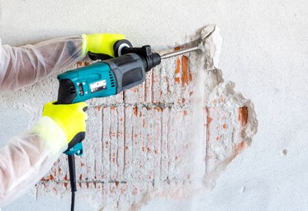 Worker removes plaster from a brick wall with a perforatorの写真素材