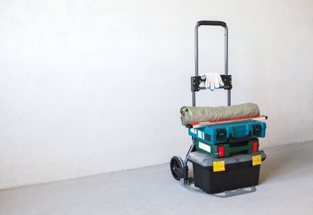Tools for repair on hand truck on the concrete floor in unfinished apartment. The set includes power tools, tool box, level, gloves and garbage bagsの写真素材