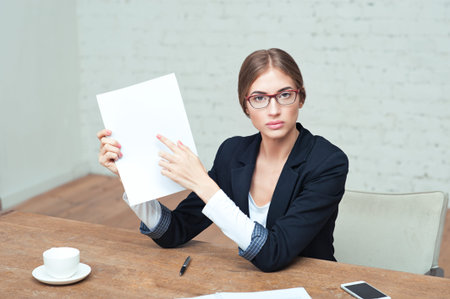 Portrait of young business woman in glasses sitting in office and showing blank white paperの写真素材