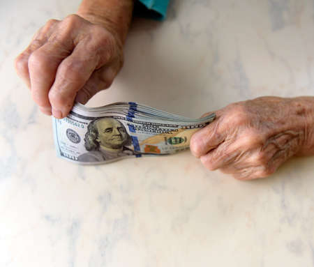 Close-up of an elderly woman's hands holding money in 100 dollar bills, compensation.の写真素材
