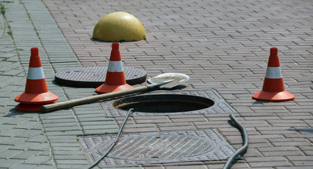 Open sewer hatch on the street near traffic cones.