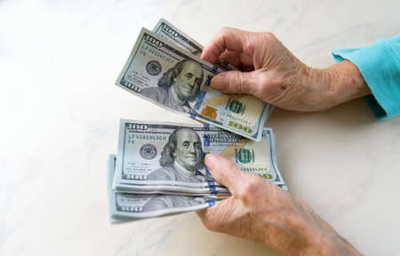 Close-up of an elderly womans hands holding money in 100 dollar billsの写真素材