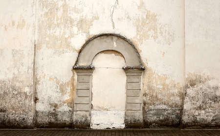 An old church wall of gray brick with a walled door on it. A buried arch in a plastered wall.の写真素材