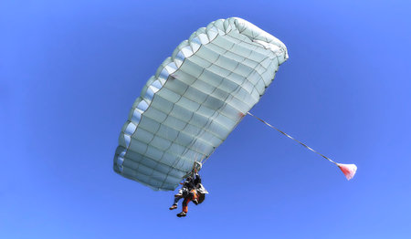White opened his parachute against the blue sky. Skydiving with an instructor.
