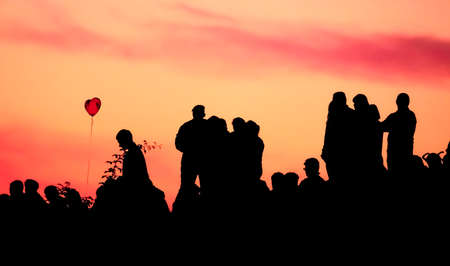 Silhouettes of people with different expressions on the embankment of the sea sunset. The crowd is watching the sunset.の写真素材