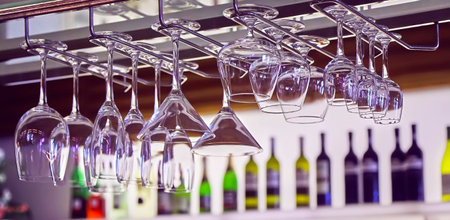Clean glasses hang against the background of wine bottles.