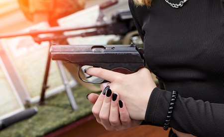 A young girl with a gun in her hands. Makarov pistol in young hands with black manicure.