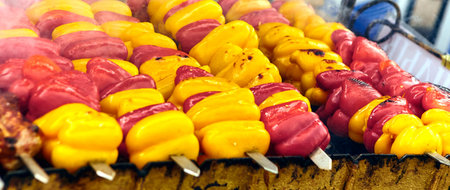 A close-up shot featuring a colorful assortment of bell peppers skewered and ready for grilling. The vibrant red and yellow peppers offer a burst of flavor, ideal for a summer barbecue in the garden.の写真素材