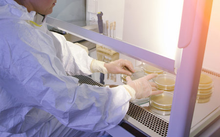Scientist in protective suit studying harmful microorganisms in biosafety cabinet