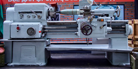 A large, industrial metalworking lathe is featured in the foreground, with its bed and headstock in...