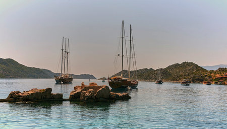 A beautiful landscape of yachts and boats docked in a calm harbor with rocky formations and lush green hills in the background. Perfect for travel, tourism, and leisure concepts.の写真素材