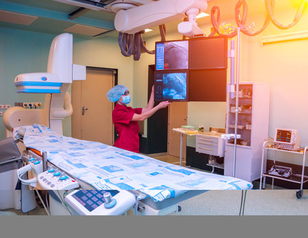 A surgeon in scrubs examines a medical display in an operating room, with the focus on the monitor and the surgeons hand. The room is equipped with advanced technology and medical equipment.の写真素材