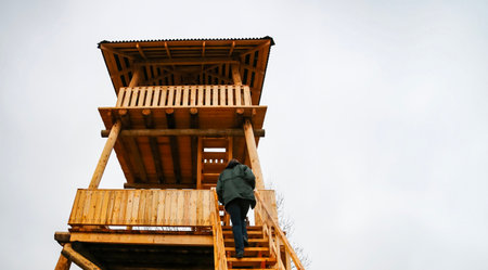 A person climbing wooden stairs toward a lookout tower in a rural area during cloudy weatherの写真素材