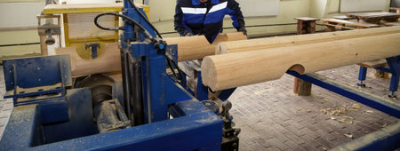 A person operates a wood lathe, shaping logs into wooden pieces in a bright carpentry workshop with...