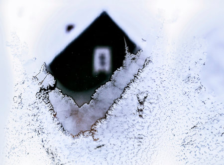 A cozy cabin obscured by frost and snow offers a glimpse of warmth in the chilly winter landscape outside.の写真素材