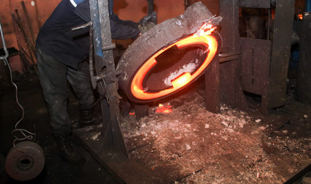 An industrial forging press machine shaping glowing hot metal disk with sparks. Made of cast iron,...