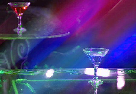 A single martini glass sits on a table in a dimly lit club, illuminated by colorful neon lights.の写真素材