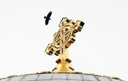 A golden cross stands prominently on a dome while a bird flies overhead, creating a tranquil atmosphere in this peaceful religious environment on a clear day.の写真素材