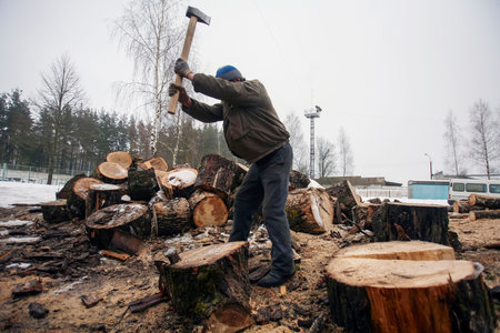 Man chopping wood in snowy environment at a lumber yard during winter