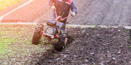 An aged red tractor plowing a vast rural field, preparing the rich soil for planting. Farmer in...