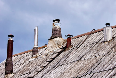 Several aging chimneys rise from the surface of a weathered roof as clouds gather in a rural landscape during late afternoon, creating an atmospheric backdrop.の写真素材