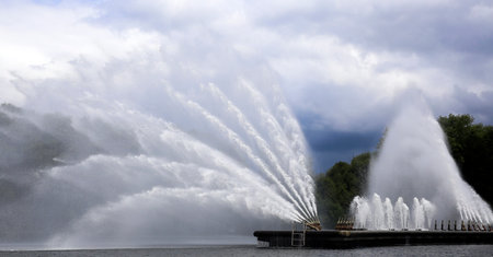 Water fountains unleash streams of water in intricate patterns, enhancing the tranquil atmosphere of the lake surrounded by trees.の写真素材