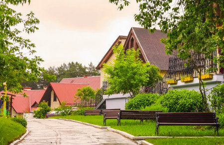 A winding path through a tranquil residential area showcases modern houses surrounded by lush vegetation, reflecting recent rain.の写真素材