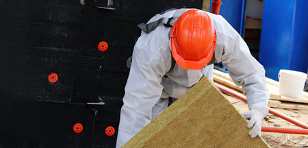 A construction worker in safety gear is placing insulation board while working on a project...